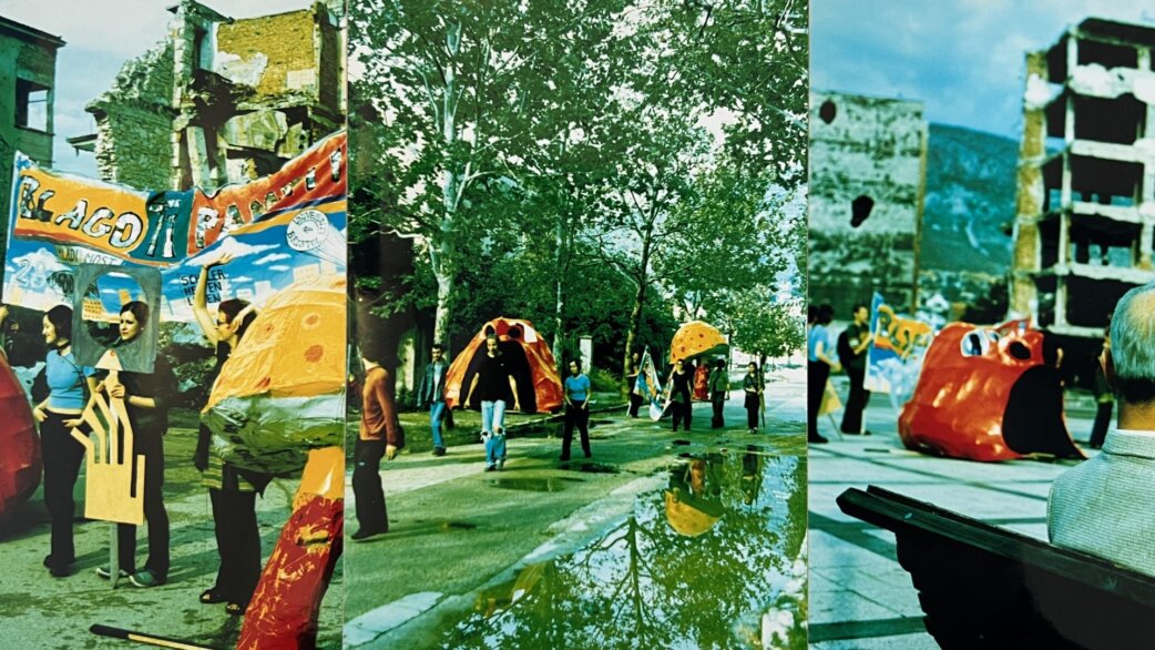 A triptych showing a colourful street parade in war-damaged Mostar, featuring people carrying vibrant recycled sculptures including orange and yellow forms, with bombed buildings visible in the background.