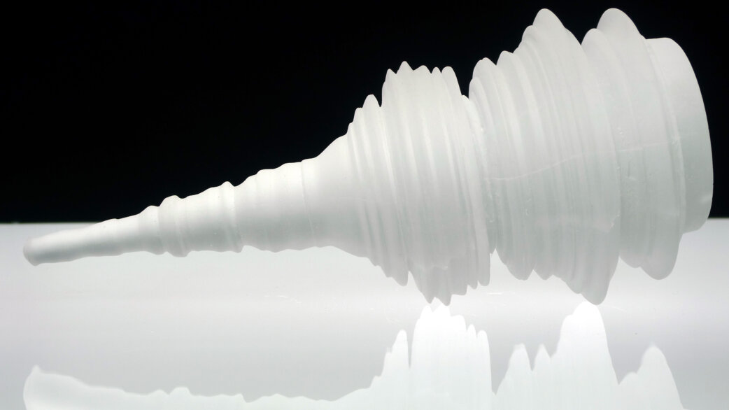A translucent white glass sculpture lying on its side, shaped like a tapered cone with ridged horizontal rings representing stock exchange data, approximately 31cm long.