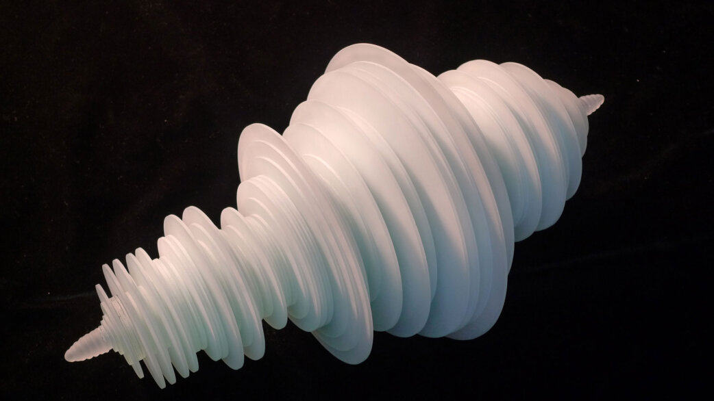 A translucent white 3D-printed sculpture resembling a spiralling shell form, created from rotated seismogram data of the 2011 Tōhoku earthquake, measuring approximately 30cm, displayed against a black background.