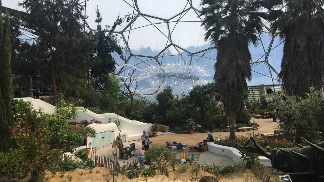 A giant inflatable E.coli sculpture, approximately 30 metres long, displayed inside the Eden Project's geodesic dome biome, surrounded by Mediterranean plants and visitors.