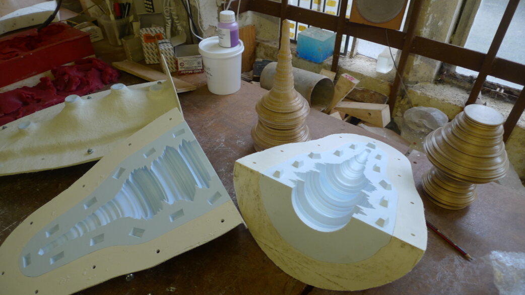 Workshop scene showing wooden turned forms and plaster moulds used for casting glass sculptures based on stock exchange data, with conical layered shapes visible on workbench.