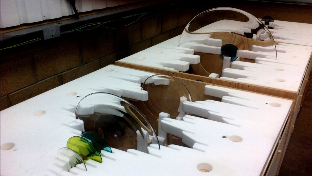 Hand-blown coloured glass roundels in green, blue and clear tones, arranged in custom white foam packaging during production of Luke Jerram's Apollo sound-wave sculpture.