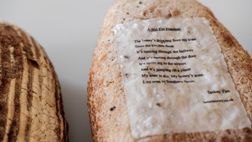 A poem titled "A Bid For Freedom" by Spikey Tim printed on edible rice paper, baked onto the underside of a crusty white loaf, with sliced bread visible alongside.